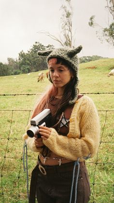 a woman standing in front of a fence holding a camera and looking at the camera