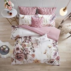 a bed with pink and white flowers on it, next to a table with a lamp