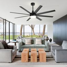 a living room with couches, chairs and a ceiling fan in front of large windows