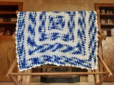 a blue and white crocheted blanket sitting on top of a wooden easel