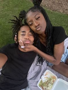 two women sitting on the ground with food in their hands and one is holding her head