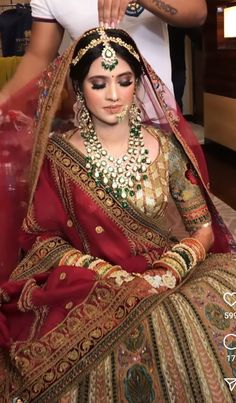 a woman in a red and gold bridal outfit getting her hair done by a man