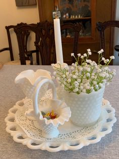 a white candle holder with flowers in it on a doily plate next to a vase