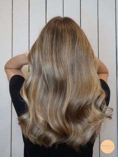 the back of a woman's head with long, blonde hair in front of a white wall