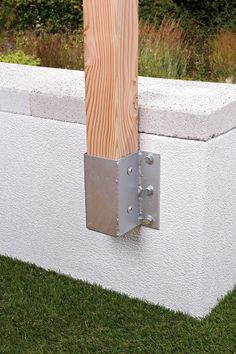 a wooden post sticking out of the side of a white wall next to green grass