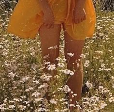 a woman in a yellow dress standing in a field of daisies and wildflowers