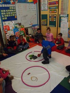 a group of children sitting on the floor in front of a white sheet with circles