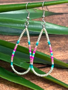 a pair of beaded earrings sitting on top of a wooden table next to green leaves