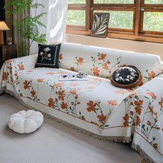 a living room with a white couch and orange flowers on the cover, next to a window