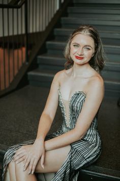 a woman in a dress sitting on the steps with her legs crossed and wearing red lipstick