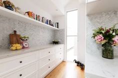 a kitchen with white cabinets and shelves filled with flowers on top of each shelf next to a wooden floor