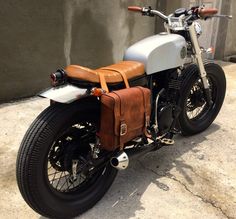 a motorcycle parked next to a building with a brown leather bag on the back seat