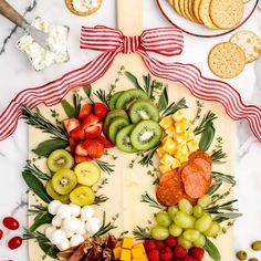 a wooden cutting board topped with fruit and veggies next to crackers on a table