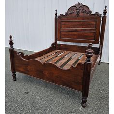 an antique wooden bed frame with carved wood slats and headboard, in front of a white wall