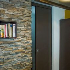 two doors are open in front of a stone wall and bookshelf on the wall