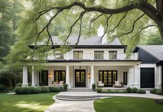 a white house with black shutters and trees in the front yard, surrounded by lush green grass