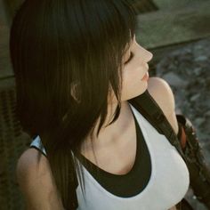 a woman with long black hair wearing a white tank top and holding a cell phone to her ear