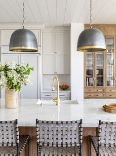 a kitchen with two pendant lights hanging from the ceiling and chairs in front of it