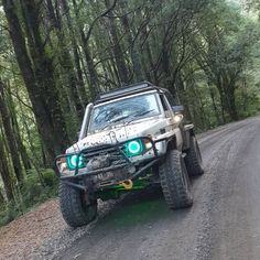 a jeep driving down a dirt road in the woods with its lights on and headlights on