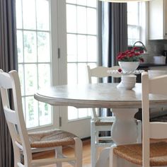 a dining room table with chairs and a vase on it in front of a window