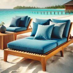 an outdoor lounge chair with blue cushions and pillows on the sand by the water's edge