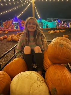 a woman sitting on top of a pile of pumpkins in a field at night