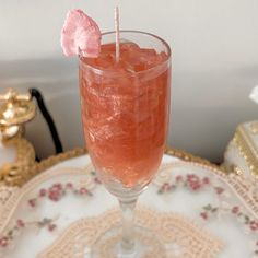 a glass filled with pink liquid on top of a white and gold tray next to a wall