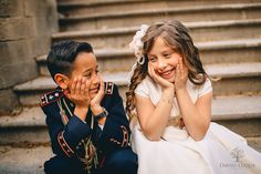 two young children sitting on the steps with their hands to their face and smiling at each other