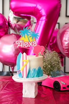 a birthday cake sitting on top of a table next to balloons and a pink car