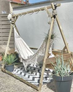 an image of a hammock hanging from a wooden frame with plants in it