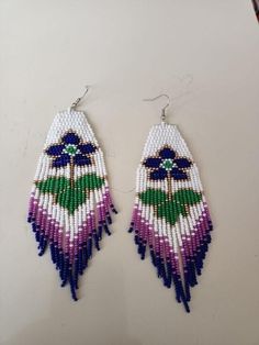 two pairs of beaded earrings with purple and green flowers hanging from the ends of them