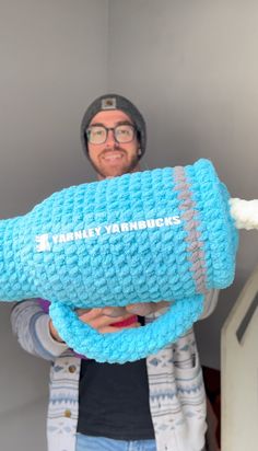 a man is holding up a blue crocheted object with the words happy yarnmen on it