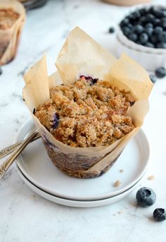 a muffin on a plate with some blueberries in the bowl next to it