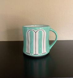 a green coffee cup sitting on top of a black table next to a white wall