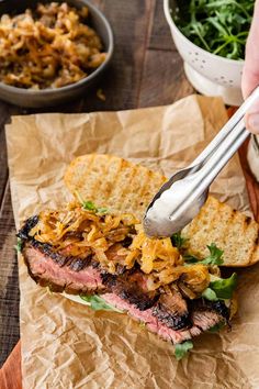 a person holding a fork over a grilled steak sandwich with onions and cheese on it