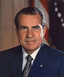 an older man in a suit and tie posing for a photo with the american flag behind him