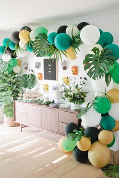 a room filled with lots of green and white balloons hanging from the ceiling next to plants