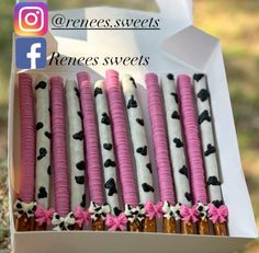 a box filled with pink and black decorated desserts next to a white paper bag