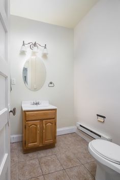 a white toilet sitting next to a wooden cabinet in a bathroom under a round mirror