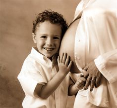 a black and white photo of a young boy holding his pregnant mother's belly