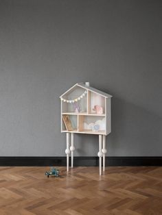 a toy house on top of a wooden floor next to a gray wall with lights