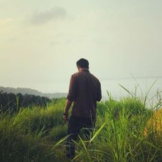 a man standing in tall grass looking out at the ocean