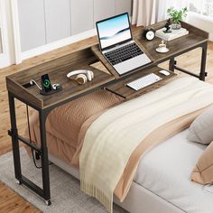 a laptop computer sitting on top of a wooden desk next to a bed with pillows