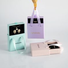 three different colored boxes with necklaces in them on a white table next to each other