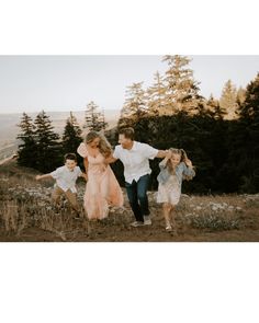 a family running through the grass in front of some trees and bushes with their arms around each other