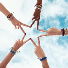 several hands making the shape of a star with their fingers in the air, against a cloudy blue sky