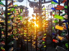 the sun is shining through bottles on display in an outdoor area with metal fence and trees