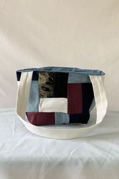 a white bag with multicolored patchwork on the front and bottom, sitting on top of a white sheet