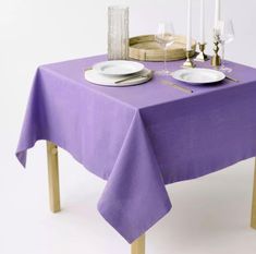 a purple table cloth with white plates and silverware on it, next to candles