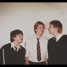 three young men standing next to each other in front of a white wall wearing ties